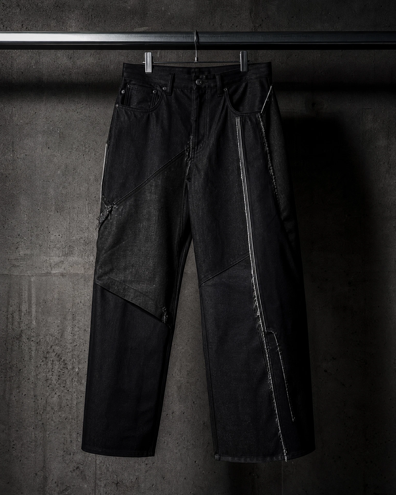 Black raw denim trousers with asymmetric panels in a concrete archive